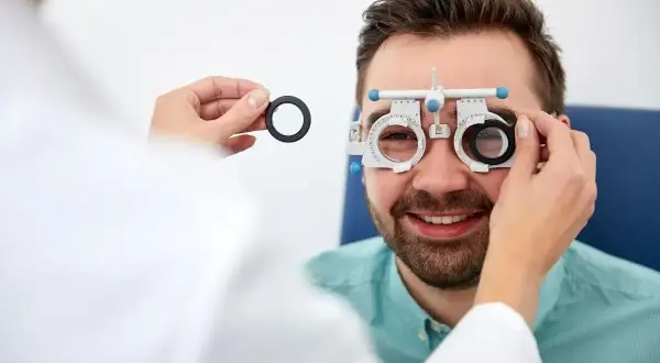 Mężczyzna uśmiecha się podczas badania wzroku. Okulista wykonuje test na zaćmę, używając oprawki próbnej.