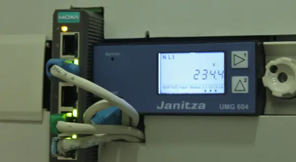 Urządzenie Janitza UMG 604 z modułem MOXA zbiera dane, umożliwiając telemetrię. Na ekranie widoczny pomiar napięcia 234.4V.