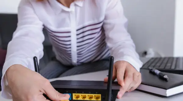Ręce podłączają kabel do routera, pokazując, jak wejść na router. Obok leży laptop i notatnik.