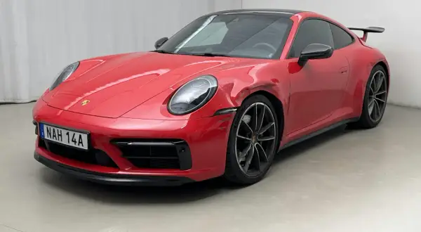 Czerwone Porsche 992 z widocznym uszkodzeniem na błotniku, stojące na szarym podłożu.