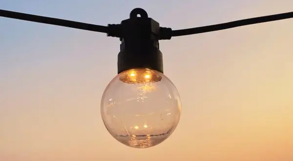 Guirlande lumineuse extérieure, une ampoule sphérique éclairée sur fond de ciel crépusculaire. La définition IP protection garantit sa résistance.