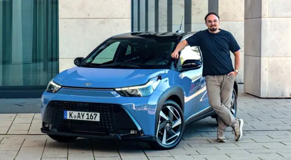 Mężczyzna opiera się o niebieską Toyotę Aygo X Hybrid.