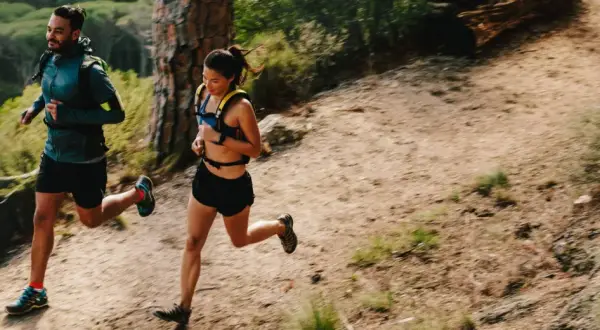 Deux coureurs s'entraînent sur un sentier de montagne, profitant d'un entraînement fractionné trail dans un paysage verdoyant.