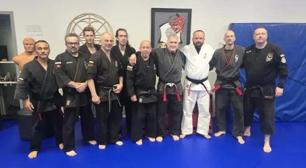 En grupp män i svarta och vita dräkter poserar på en blå matta. De är en del av en kenpo karate-klubb.