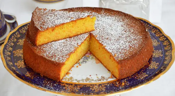 Una deliziosa torta carote e mandorle, spolverata di zucchero a velo, servita su un elegante piatto decorato.