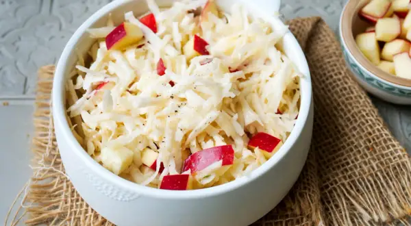 Frischer sellerie salat mit roten Apfelstücken, garniert mit schwarzem Pfeffer, serviert in einer weißen Schüssel auf Jute.