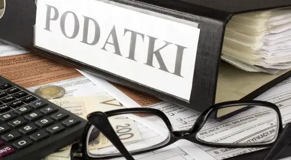 Segregator z napisem "PODATKI", okulary, kalkulator i pieniądze. Kto to jest rezydent podatkowy? To osoba, która musi rozliczyć się z dochodów.