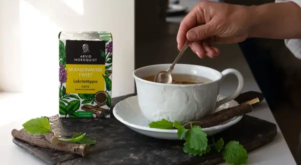 En hand rör om i en kopp te. Bredvid står en ask med Skandinavisk Twist Lakritstäppa, som ger te smak.