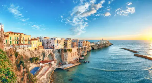 San Mennaio, un borgo sul mare con case colorate aggrappate alla scogliera, baciato dal sole al tramonto.