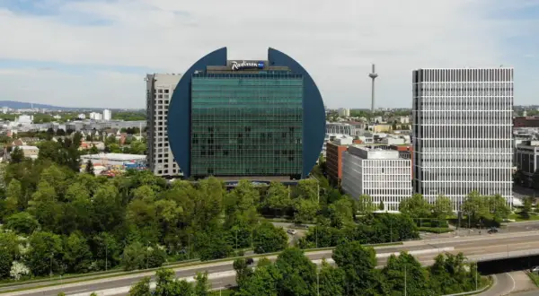 Charakterystyczny budynek Radisson Blu we Frankfurcie, otoczony zielenią, obok nowoczesnych wieżowców.