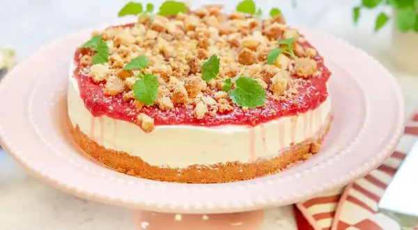 En krämig rabarber cheesecake med smulig topping och färska myntablad, serverad på ett rosa tårtfat.