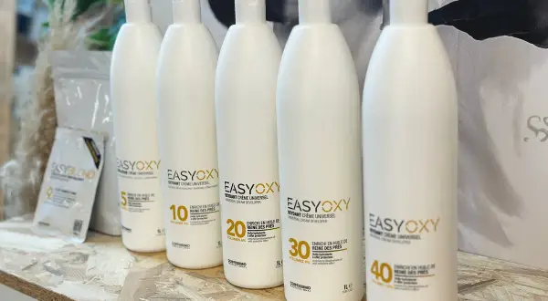 Cinq bouteilles d'oxydant crème universel, dont une de 40 volumes, sont alignées. Ce peroxyde d'hydrogène est enrichi en huile de reine des prés.