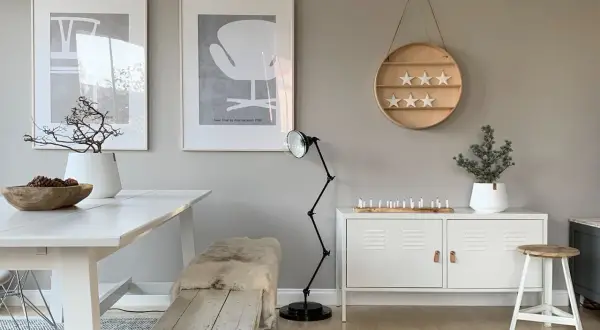 Ein Esszimmer im skandinavischen Stil mit einer warmen grau farbpalette. Ein weißer Tisch, eine Holzbank mit Schaffell und Kunstwerke an der Wand.