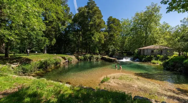 Un refrescante pozo do boi con aguas cristalinas, rodeado de exuberante vegetación y una antigua edificación de piedra.