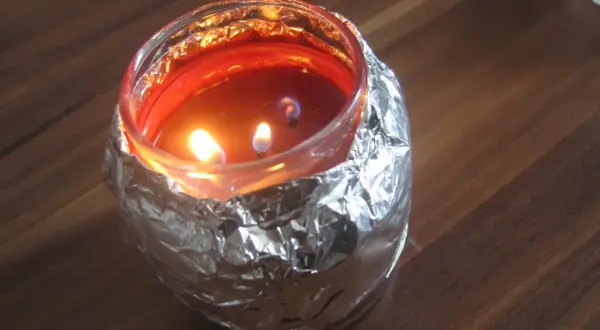 Płonąca świeca w szklanym naczyniu, owiniętym folią aluminiową, tworząc efekt tunelowania świecy.