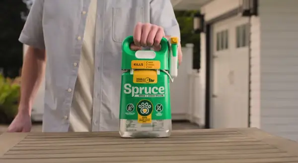 Mężczyzna trzyma butelkę środka "Spruce" - orkan na chwasty. Skutecznie zwalcza chwasty, trawy i mech.
