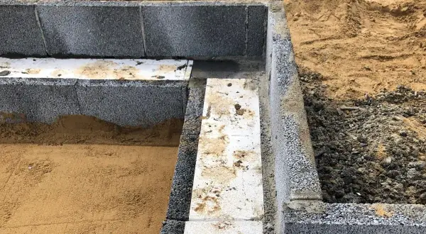 Grunden byggs med lecablock. Sand och grus syns runt den pågående murningen.