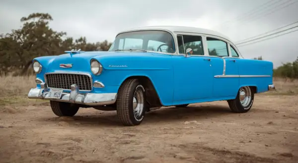 Blå och vit cheva 56 står parkerad på en grusväg. Bilen har kromade detaljer och vita däcksidor.