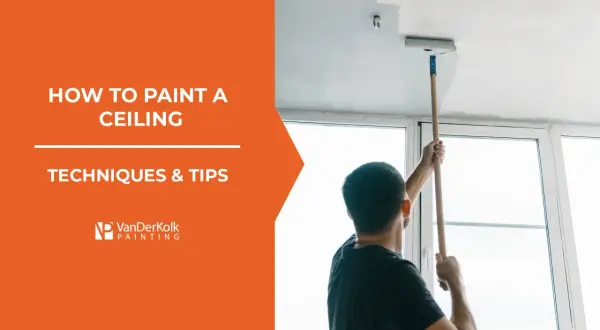 Learn how to paint a ceiling with this guide. A man uses a roller on an extension pole to apply white paint to a ceiling.