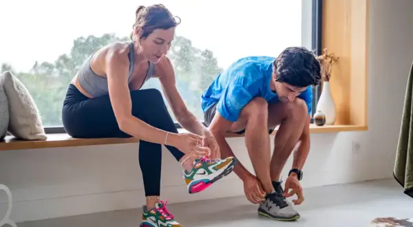 Un couple se prépare pour reprendre le sport, enfilant leurs chaussures de course près d'une fenêtre lumineuse.