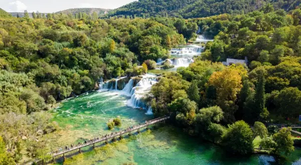 Atemberaubende Wasserfälle im Krka Nationalpark, Kroatien. Eine Holzbrücke führt Besucher über das smaragdgrüne Wasser.