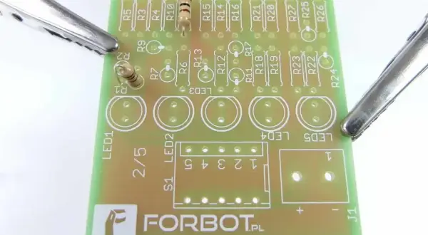 Płytka drukowana z elementami elektronicznymi, w tym rezystorami i diodami LED. Krokodylki podtrzymują płytkę, gotową do lutowania. Widać napis FORBOT.PL, sugerujący projekt z użyciem **tinol**u.