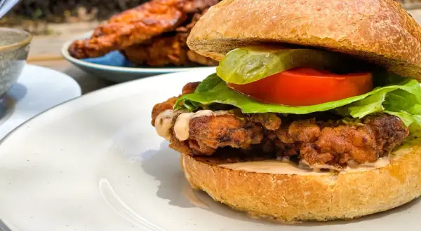Burger maison au poulet croustillant et juteux, garni de laitue, tomate et cornichon.