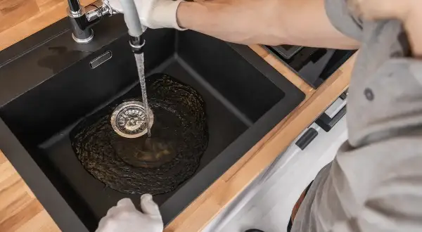 Wasser fließt in die Spüle, der Abfluss gluckert aber nicht verstopft. Ein Mann mit Handschuhen prüft den Wasserfluss.