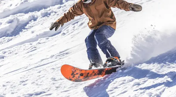 Mężczyzna na desce snowboardowej męskiej zjeżdża po ośnieżonym stoku, tworząc obłok śniegu.