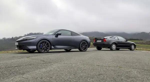 Due coupé Honda, una moderna e una classica, si incontrano su una strada di campagna. La nuova Honda Prelude 2026, grigio scuro, spicca accanto alla sua antenata.