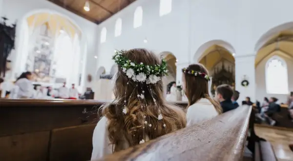 Dwie dziewczynki w wiankach siedzą w kościele podczas komunii.
