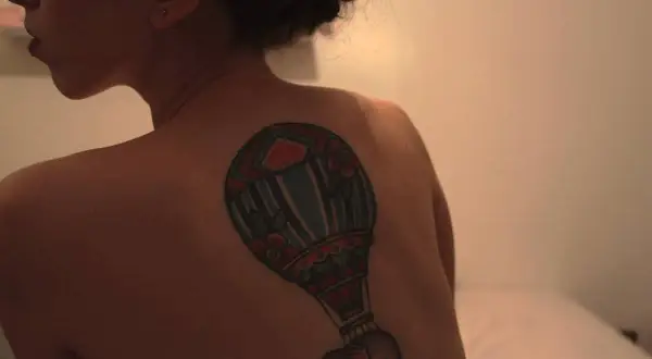 Kolorowy tatuaż balon z małym słoniem na plecach kobiety.