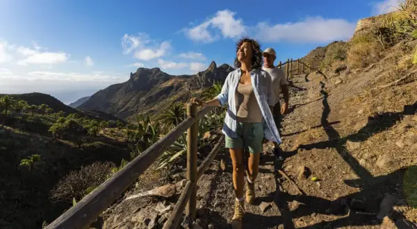 Ett par njuter av en vacker la gomera vandring i solsken, med dramatiska berg och palmer i bakgrunden.