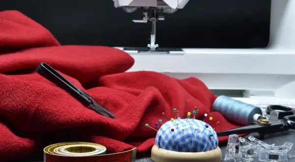 Czerwony materiał, maszyna do szycia, szpilki, nici i miarka – wszystko, co można uszyć, czeka na kreatywne pomysły.