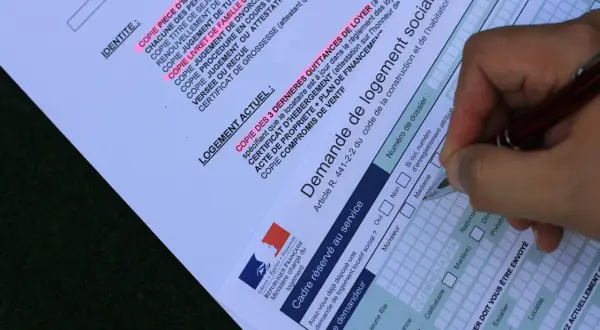 Formulaire de demande de mutation pour un logement social. Un stylo remplit les champs d'une demande de logement social.