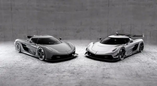 Dwa lśniące Koenigsegg Jesko, jeden szary, drugi srebrny, stoją obok siebie na betonowym tle.