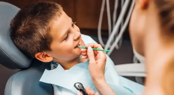 Chłopiec u dentysty, który bada jego zęby. Lekarz delikatnie dotyka jego dziąsła, sprawdzając, czy nie ma żadnej dziury w dziąśle.