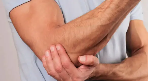 En man håller sin armbåge, som om han har ont i underarmen ovansida.