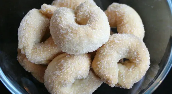 Un gruppo di taralli dolci, ricoperti di zucchero cristallino, in una ciotola di vetro.