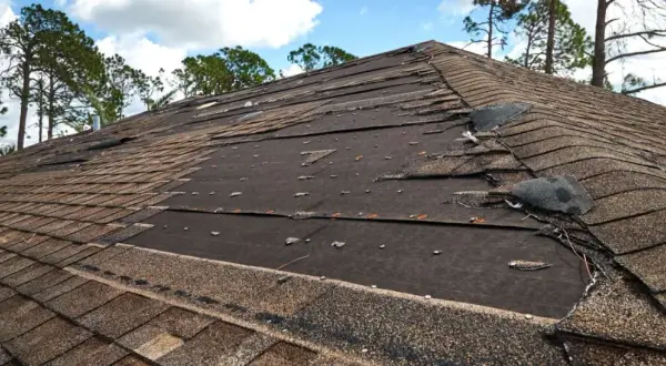 Damaged asphalt shingle roof repair needed. Many shingles are torn, lifted, or missing, exposing the underlayment.