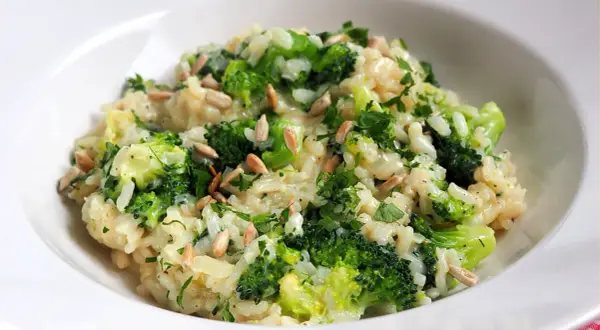 Kremowe risotto z brokułami, posypane słonecznikiem i natką pietruszki, podane w białej misce.