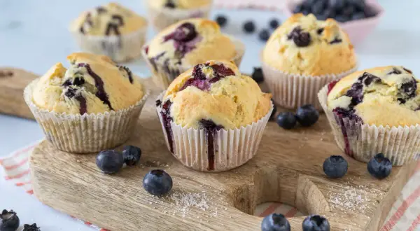 Frisch gebackene Blaubeermuffins, die nach den besten Muffin Rezepten aussehen, liegen auf einem Holzbrett.