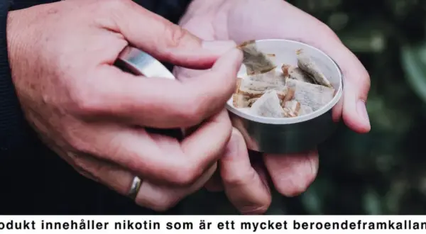 Händer tar en prilla snus ur en dosa. En perfekt dag för snusets dag, men kom ihåg nikotinets beroendeframkallande natur.