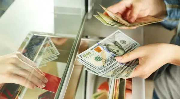 Wymiana dolarów w kantorze bez dowodu. Dłonie przekazują sobie banknoty 100 USD.