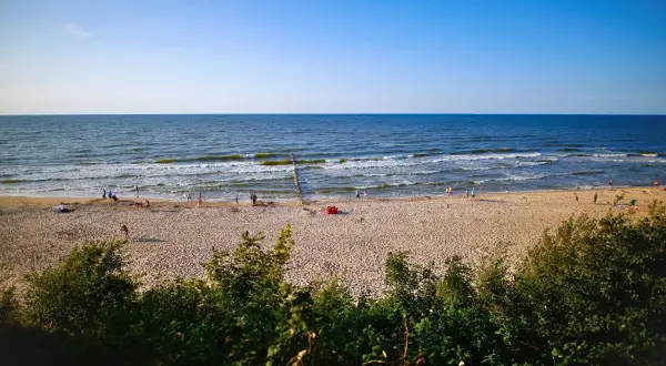 Słoneczna plaża, morze i ludzie spacerujący brzegiem. Dziwnówek atrakcje to idealne miejsce na letni wypoczynek.