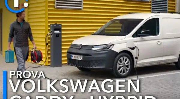 Un uomo porta cavi per caricare il Volkswagen Caddy eHybrid, un furgone bianco parcheggiato vicino a una stazione di ricarica.