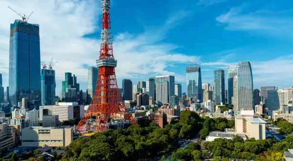 Tokio Tower góruje nad nowoczesnym miastem z wieżowcami w budowie i zielonymi drzewami.