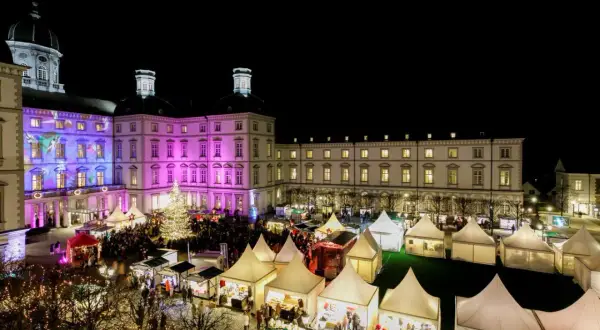 Festlicher weihnachtsmarkt schloss bensberg mit beleuchtetem Baum, bunten Lichtern und vielen Besuchern in Zelten.