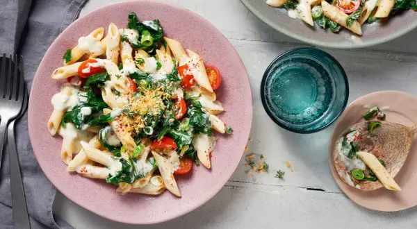 Penne mit Spinat und cremiger Sauce auf einem rosa Teller, garniert mit Kirschtomaten und Kräutern.