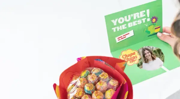 En person håller upp ett kort med texten "YOU'RE THE BEST" och en bild på sig själv. Bredvid syns en bukett med Chupa Chups-klubbor, en fin godis present diy.